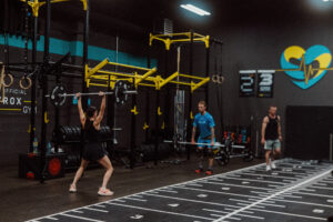 People working out in a functional fitness gym with yellow rig equipment, barbells, and gymnastics rings.